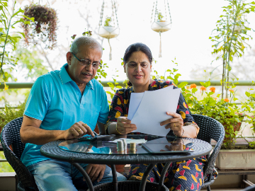 Senior Indian asian couple accounting, doing home finance and checking bills with laptop, calculator and money also with piggy bank while sitting on sofa couch or table at home